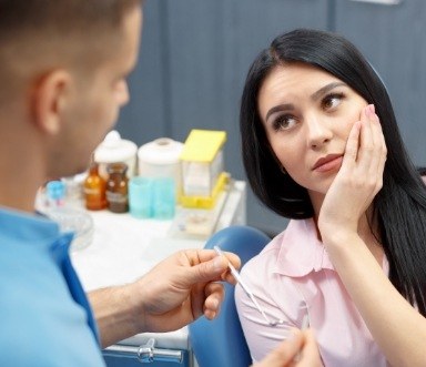 Woman holding cheek in pain discussing warning signs of oral cancer