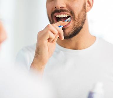 Man brushing teeth in front of mirror, caring for his dental implants