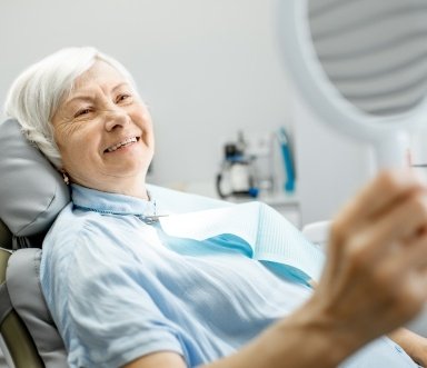 Woman looking at smile after dental implant denture placement