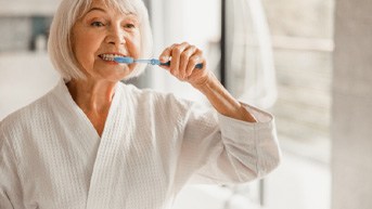 older woman brushing teeth in bathroom   