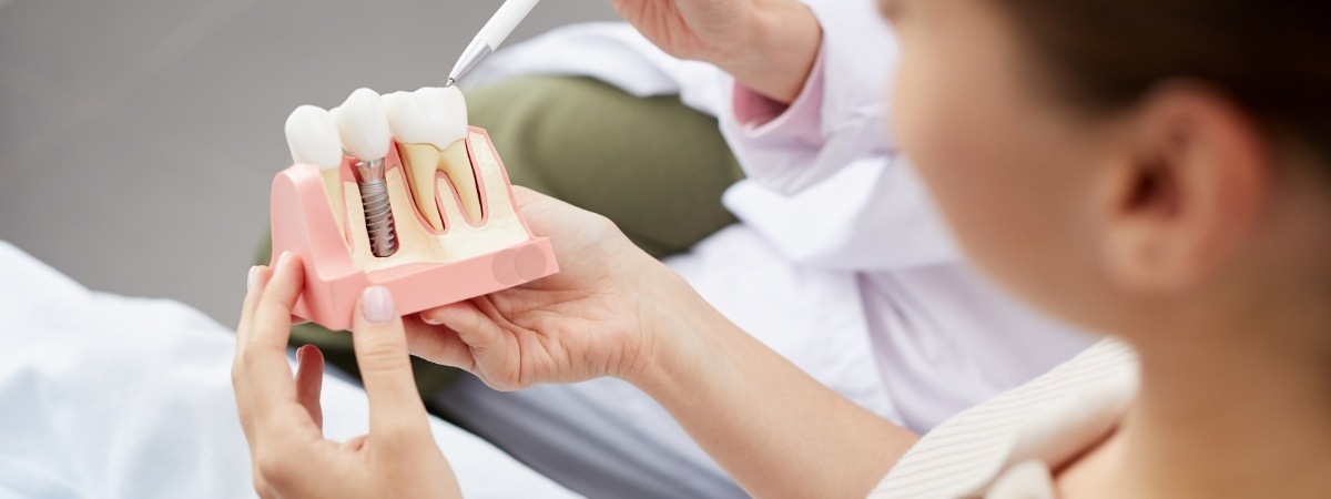 Dentist and patient looking at model of dental implant supported dental crown
