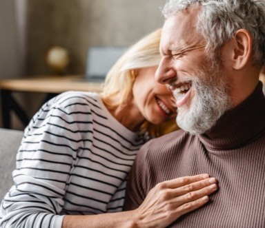 Man and woman laughing together after dental implant tooth replacement