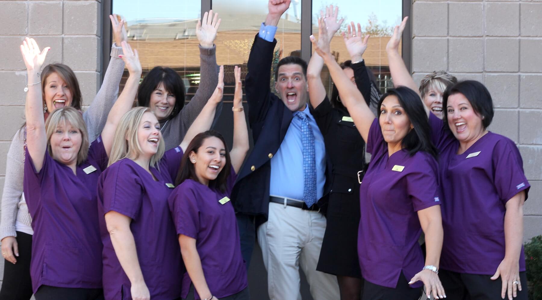 Burlington dentist and team members raising their hands in front of dental office building
