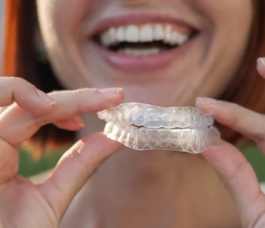 Smiling person holding a set of nightguards for bruxism