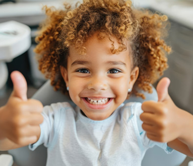Child smiling and giving two thumbs up during appointment 