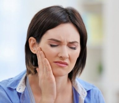 Woman in need of dental care holding cheek in pain