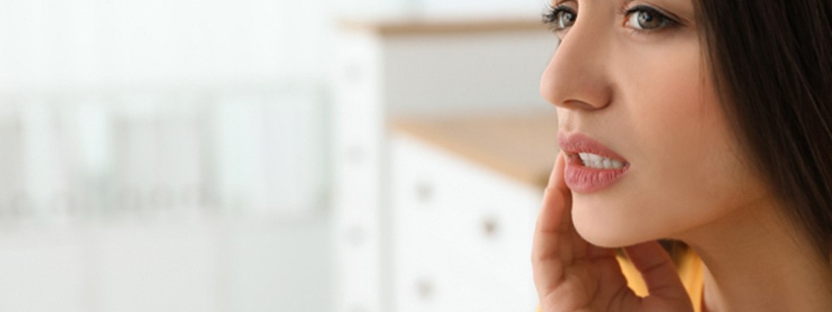 Woman at home rubbing jaw and looking worried