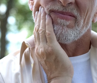 Bearded man outside frowning and rubbing jaw