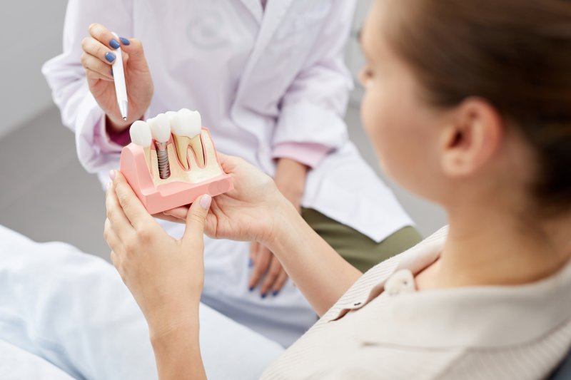 Patient talking to their dentist, who is holding a model of a dental implant
