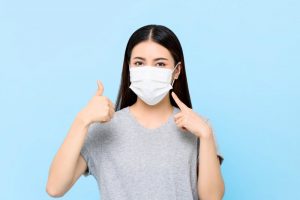 young woman wearing and pointing to a face mask